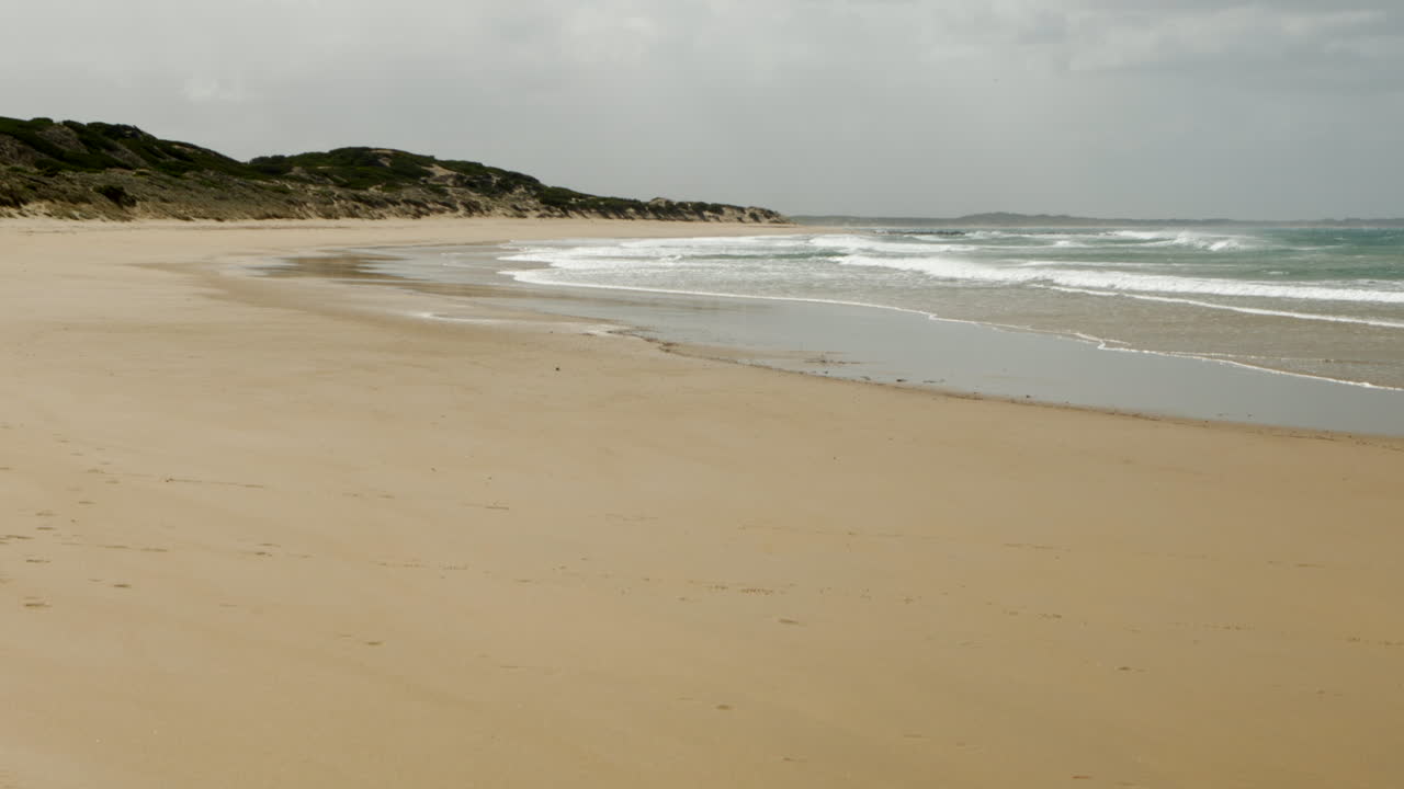 바람이 휘몰아치는 고립된 해변에는 주변에 사람이 없고 흠집 하나 없는 황금빛 모래가 있습니다.