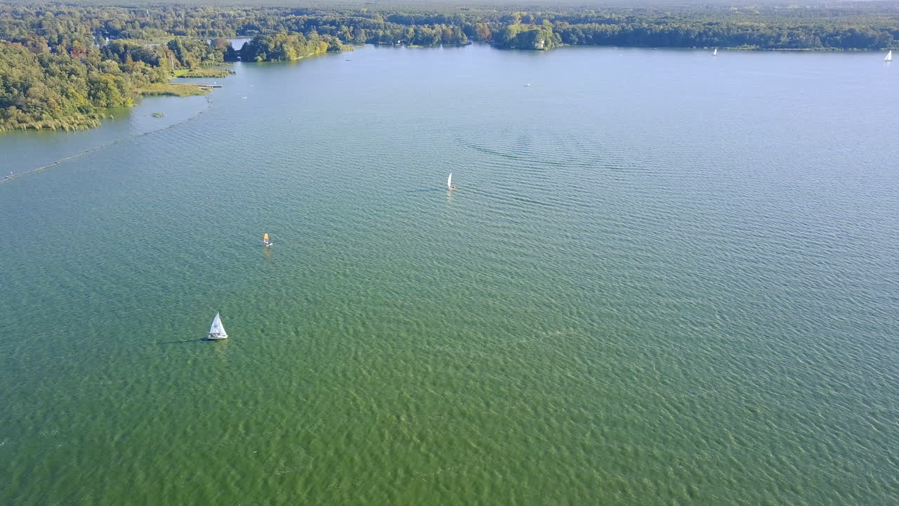 drone volando sobre un lago con veleros y windsurfistas proyectando grandes sombras