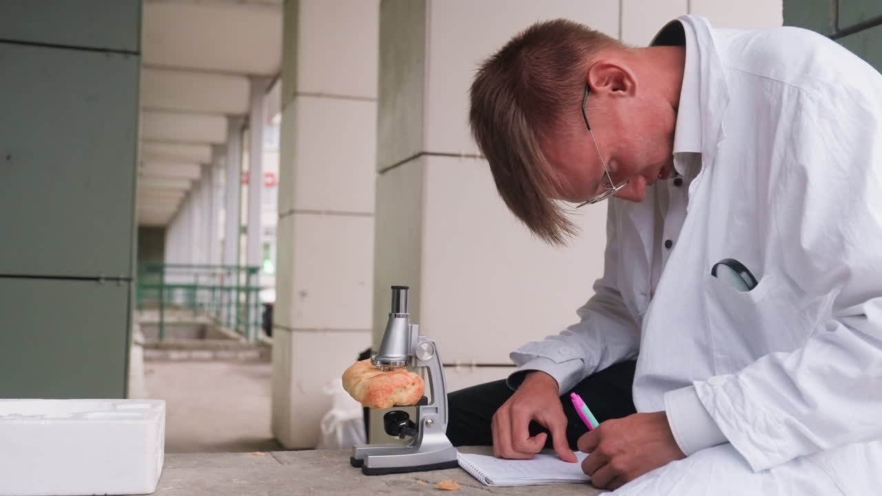 Scientific researcher in white coat carefully examining pastry through microscope in outdoor setting, reflecting curiosity, focus, and scientific observation while jotting notes with pen