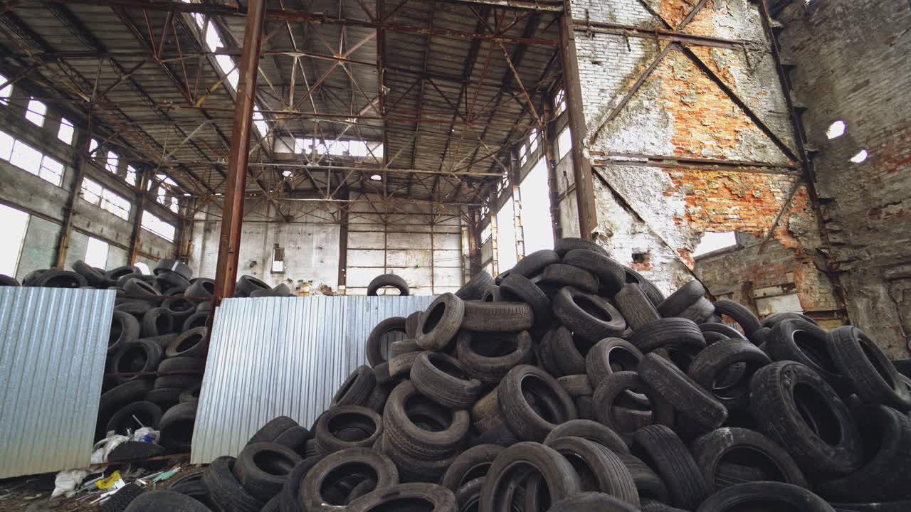 Landfill of used automobile tires on the old abandoned plant inside. Huge piles of black waste wheels from different vehicles. Motion bottom up