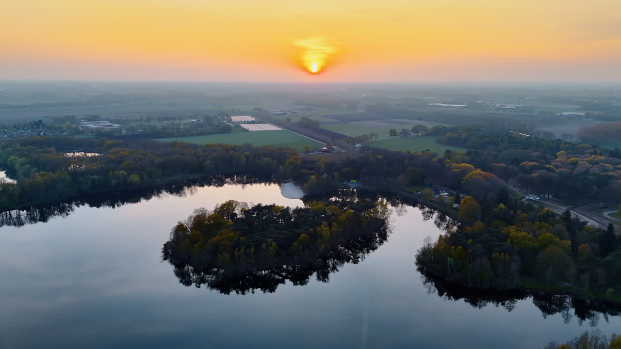 Sunset over Dutch landscape with lake. Aerial view captures a beautiful sunset over a serene lake in the Netherlands, surrounded by lush greenery and fields