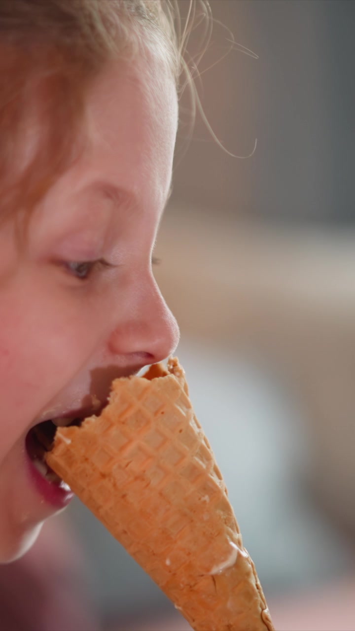 Close up of young girl enjoying ice cream cone repeatedly bringing it to her mouth and taking bites. sequence captures texture details of both waffle pattern on wafer and soft lighting