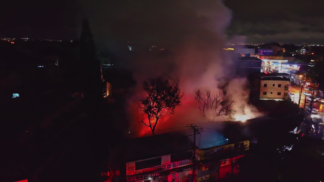 Thick Smoke Rising From Industrial Warehouse Fire At Night In Santiago de los Caballeros, Dominican Republic. aerial shot