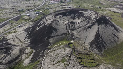 drone video tilting up revealing the grabrok crater with a small hiking path leading to the rim of this dormant volcano in iceland