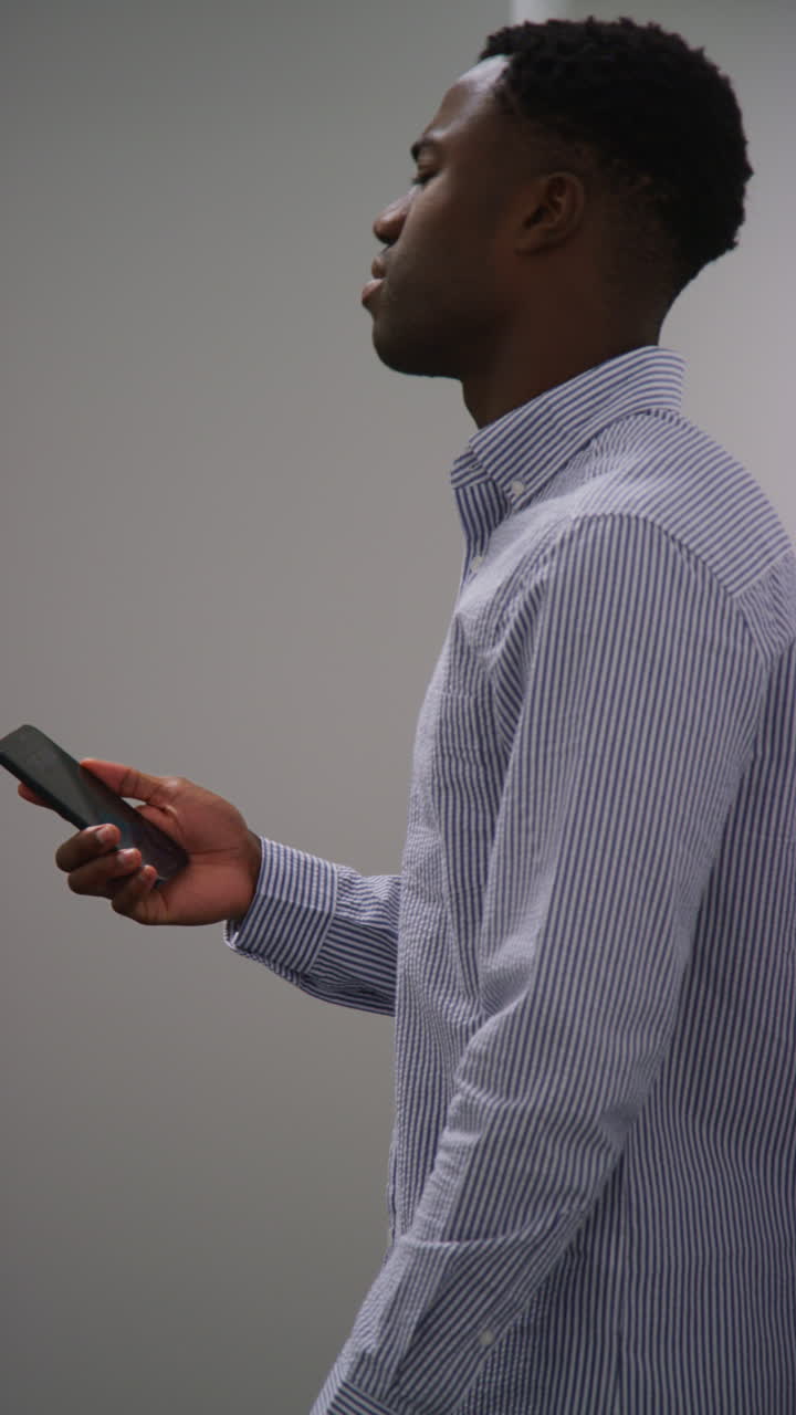 Vertical Video Of Young Businessman In Office Looking At Message With Bad News On Mobile Phone And Leaning Against Wall Looking Unhappy And Depressed 1