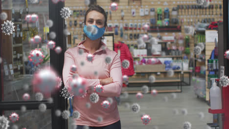 multiple covid-19 cells floating against portrait of caucasian woman wearing a mask at the shop