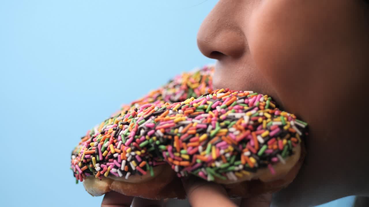 Asiatisk jente spiser sjokoladedonut med blå bakgrunn, sideprofil og sakte film