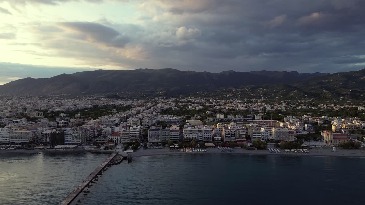 Filmagem aérea com movimento de câmera para a direita da paisagem urbana de Kalamata, nuvens sobre montanhas ao fundo, vista do mar em 4K.