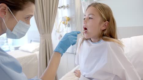 Caucasian-female-doctor-in-mask-and-gloves-checking-throat-of-girl-patient-in-hospital,-slow-motion