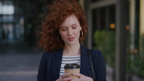 portrait young beautiful red head business woman smiling enjoying successful lifestyle holding coffee wind blowing hair in urban outdoors background ambition success