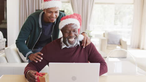 Feliz-Padre-Afroamericano-Con-Regalo-E-Hijo-Teniendo-Videollamada-Navideña-Con-Computadora-Portátil,-Cámara-Lenta