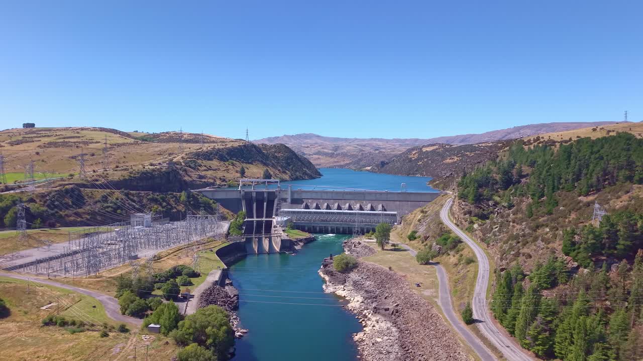 Low reverse aerial rising above the Clutha River to reveal the full Roxburgh hydro dam and scenic Roxburgh Lake in Central Otago, New Zealand