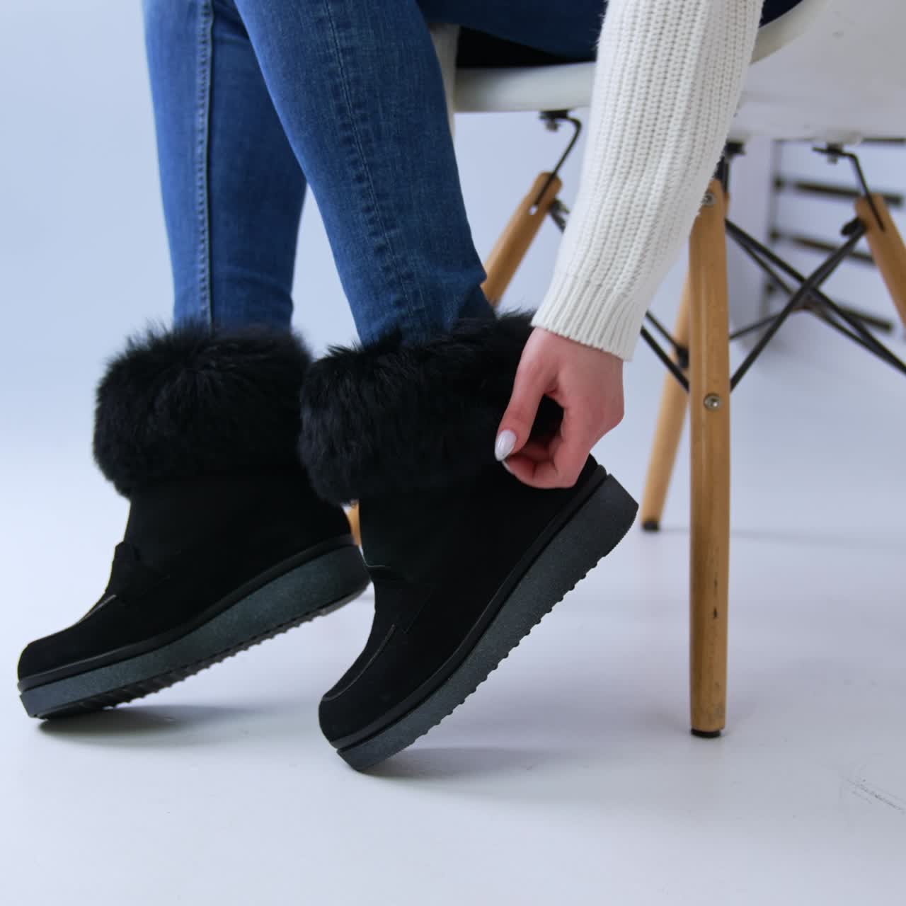 Comfortable winter boots on plain soles with artificial fur on top. Model sitting on the chair touching the footwear. White backdrop