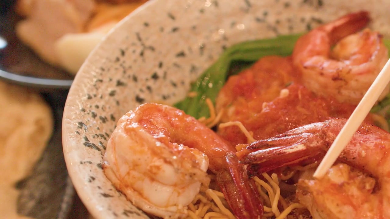 Primo piano di bacchette che sollevano un grande gambero grigliato da una ciotola di noodles Shan birmani