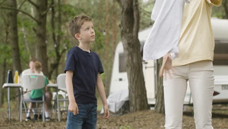 little boy helping her mother to hang out washing clothes on clothesline at the camping in the forest