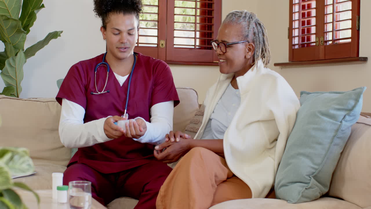 Caregiver in scrubs assisting senior woman at home, sharing warm conversation