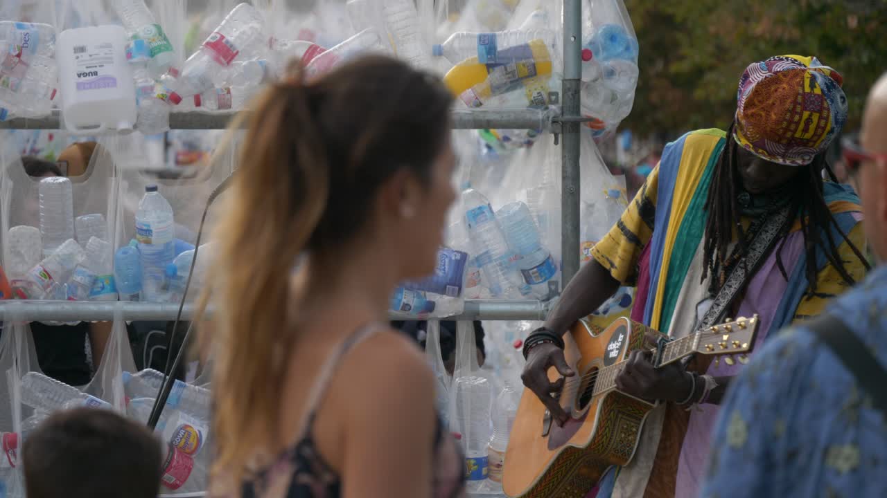 Woman Watches Street Musician Play Guitar, Plastic Bottle Collection
