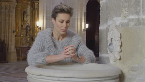 woman makes cross sign by holy water font in church close up