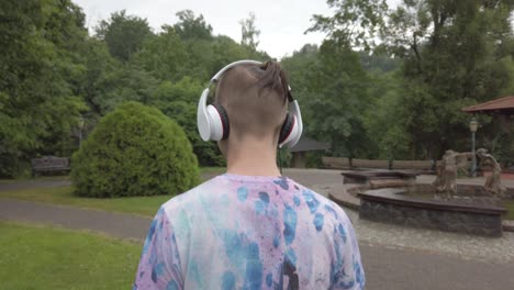 teenager boy listen to the music with the headphones on while doing a walk, the camera man follows from the back, 24 frames per second at 4k