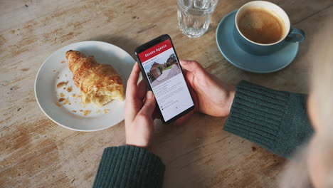 close up of woman looking at realtors property app on mobile phone in cafe