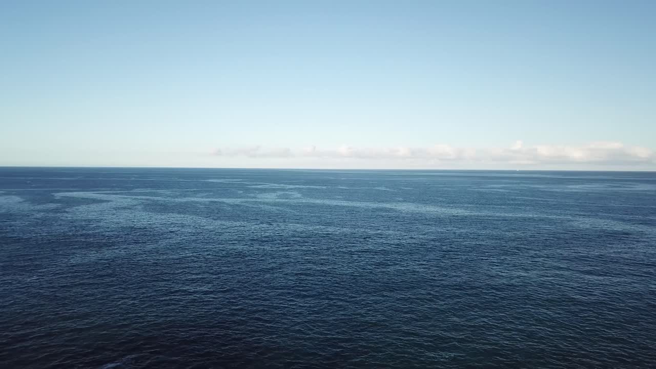 A peaceful tropical bay with clear blue water stretches toward steep cliffs and a palm-lined shoreline. Captured from above, the scene highlights natural beauty and coastal tranquility.