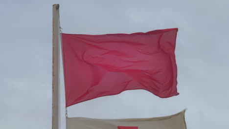 Rote-Fahne-Weht-An-Einem-Windigen,-Stürmischen-Tag-Am-Strand