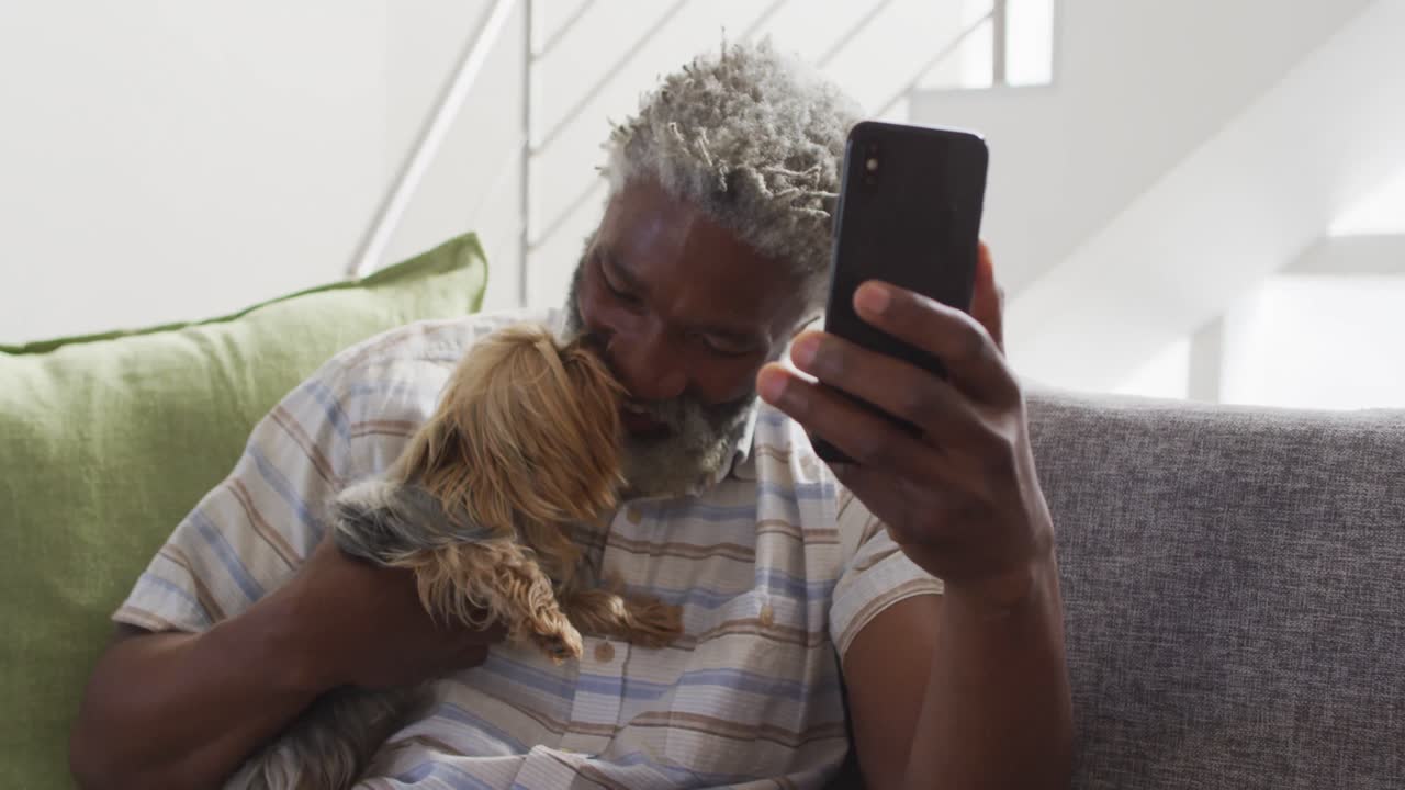 Senior man holding his dog having a video chat on smartphone at home