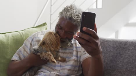 senior man holding his dog having a video chat on smartphone at home
