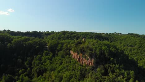 drone rising on top of a green valley, with summer woodlands, some rocky mountains and a blue sky, italy, 4k aerial