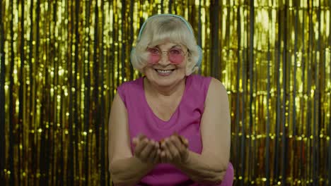 happy mature old woman laughing, blowing confetti glitters, celebrating birthday, winning lottery