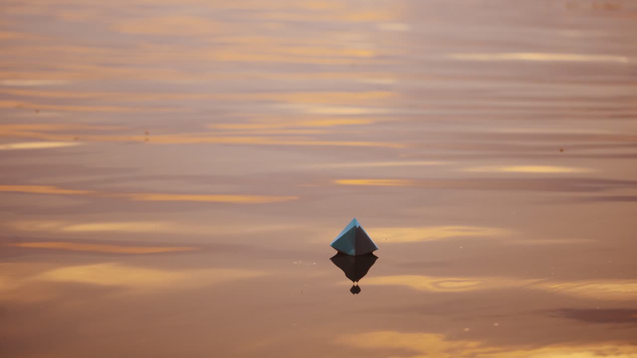 Paper boat on evening water. White origami boat floating alone on light waves on water surface at sunset.