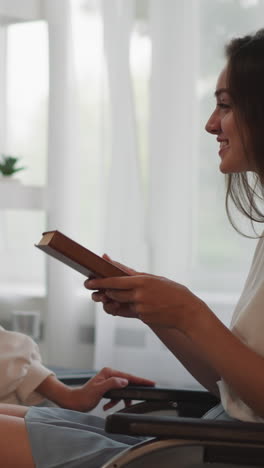 una mujer con discapacidad se sienta en una silla de ruedas examinando un libro dado por su novia. parejas lesbianas felices sonríen discutiendo una novela romántica en un plano cercano compartido