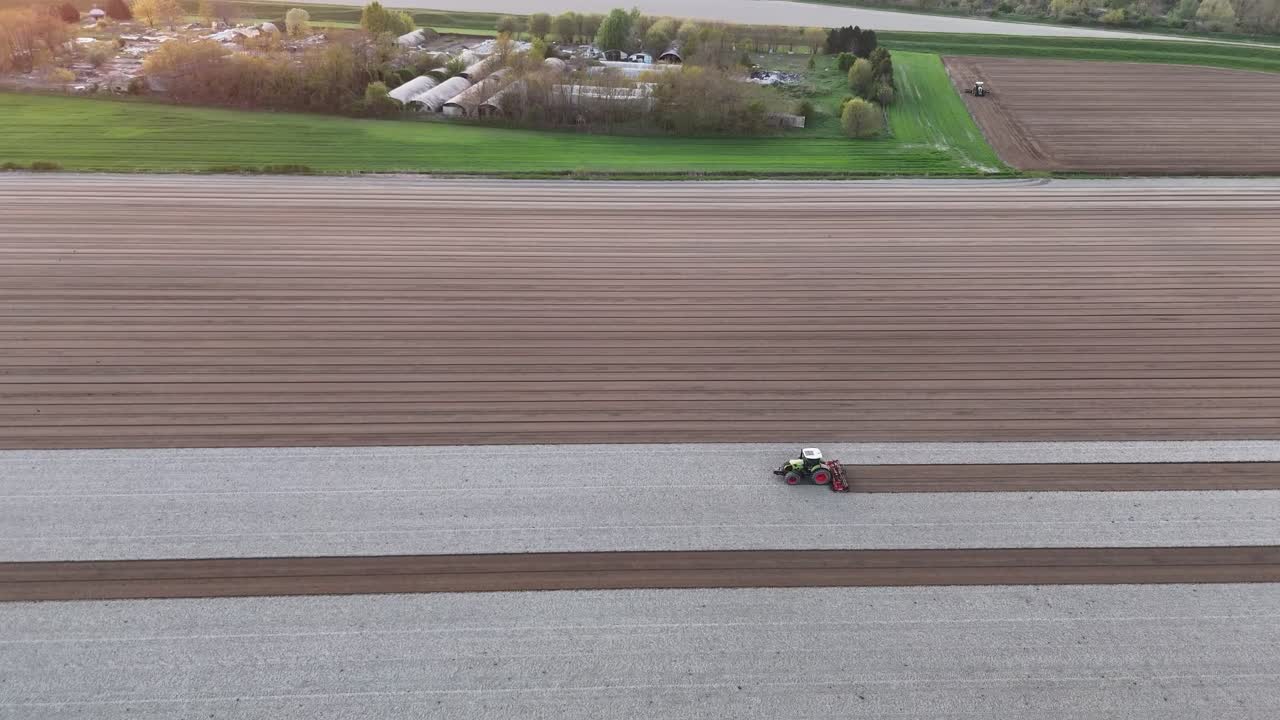 Ttractor working across parallel crop rows in the Po Valley, Italy, with rural buildings and trees in the background, highlighting mechanized field preparation in a major agricultural region