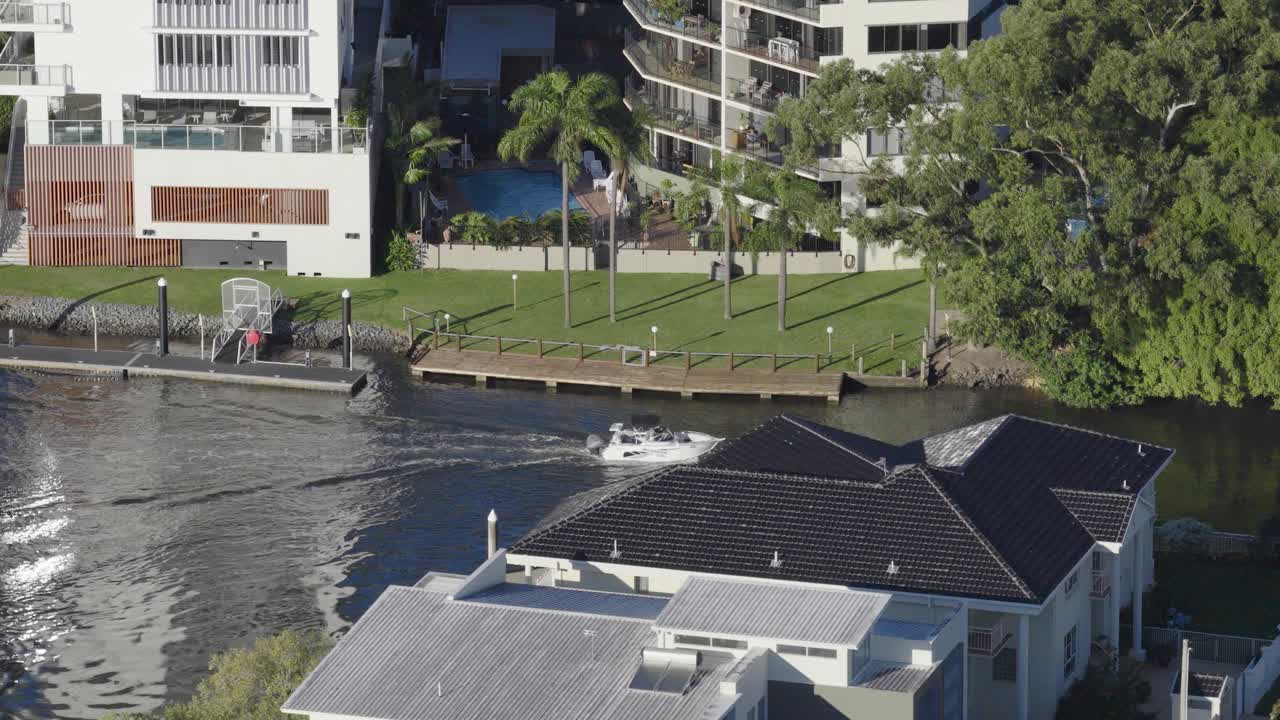 Aerial footage of Broadbeach, Gold Coast, showing waterfront homes, lush greenery, and a boat on a sunny day
