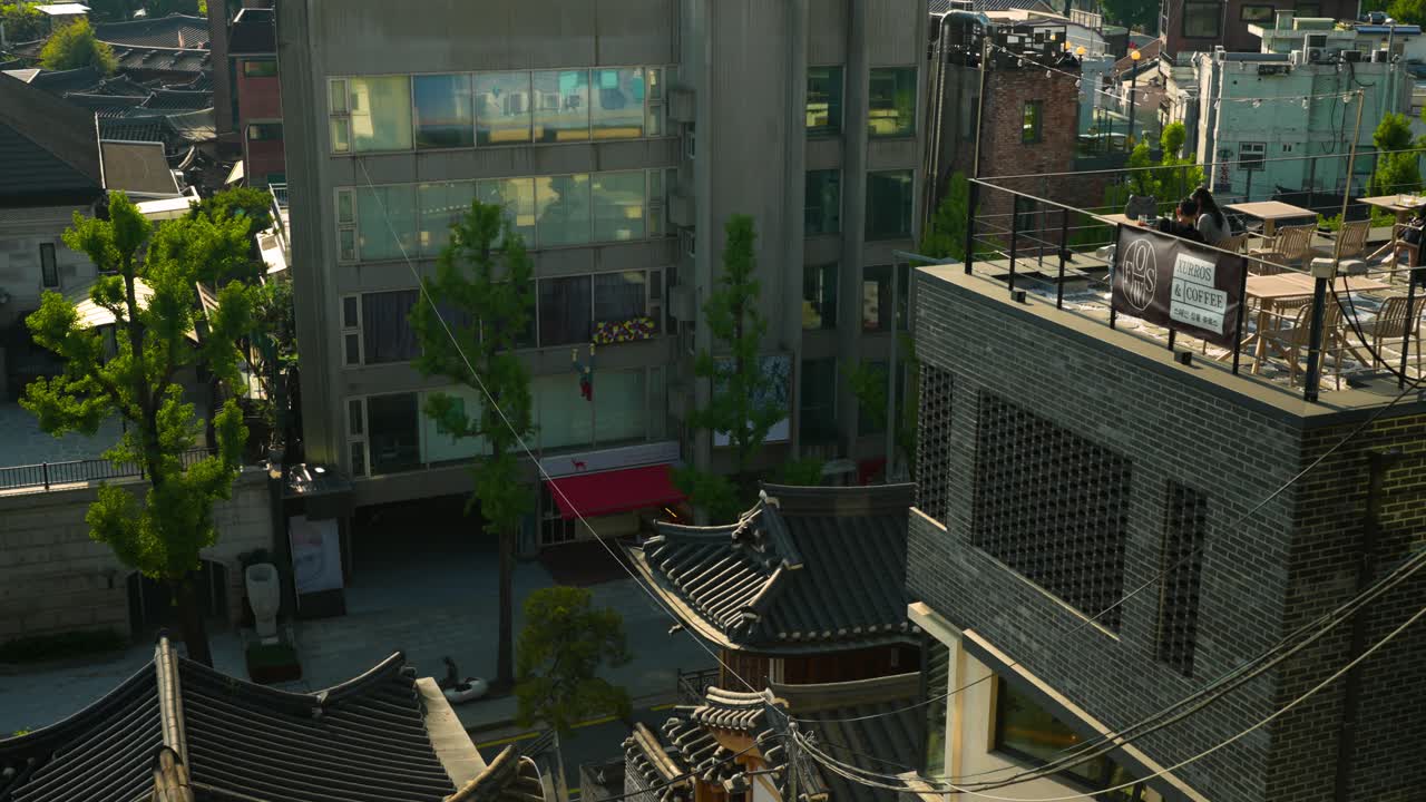 Contemporary buildings and rooftop cafes blend with traditional hanok rooftops along a vibrant street in Bukchon Hanok Village, Jongno-gu, Seoul