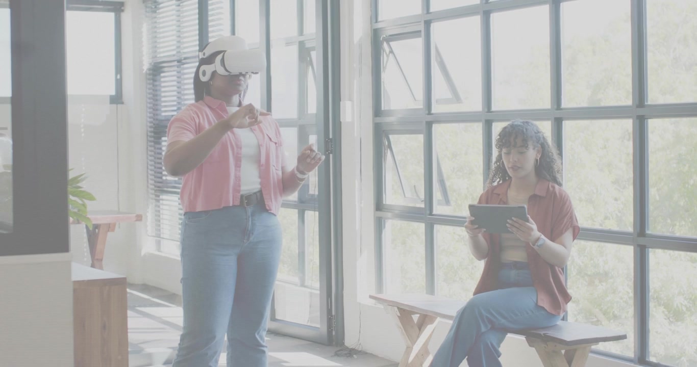 Stojący użytkownik zakładający gogle VR, gestykulujący, podczas gdy siedzący użytkownik testuje tablet, a interfejs użytkownika technologii reaguje