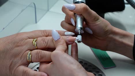 precision nail care: expert manicurist using electric drill for flawless nail finish in beauty salon