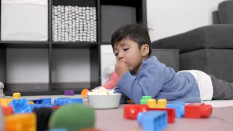 Niño-Mexicano-De-Dos-Años-Comiendo-Palomitas-De-Maíz-Tirado-En-El-Suelo-Y-Viendo-La-Televisión