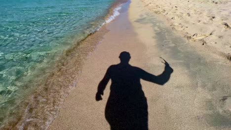 Silueta-Sombra-Del-Hombre-Quitándose-Las-Gafas-De-Sol-Y-Caminando-En-La-Playa-De-Arena-A-Lo-Largo-De-La-Costa-De-Agua-De-Mar-Turquesa