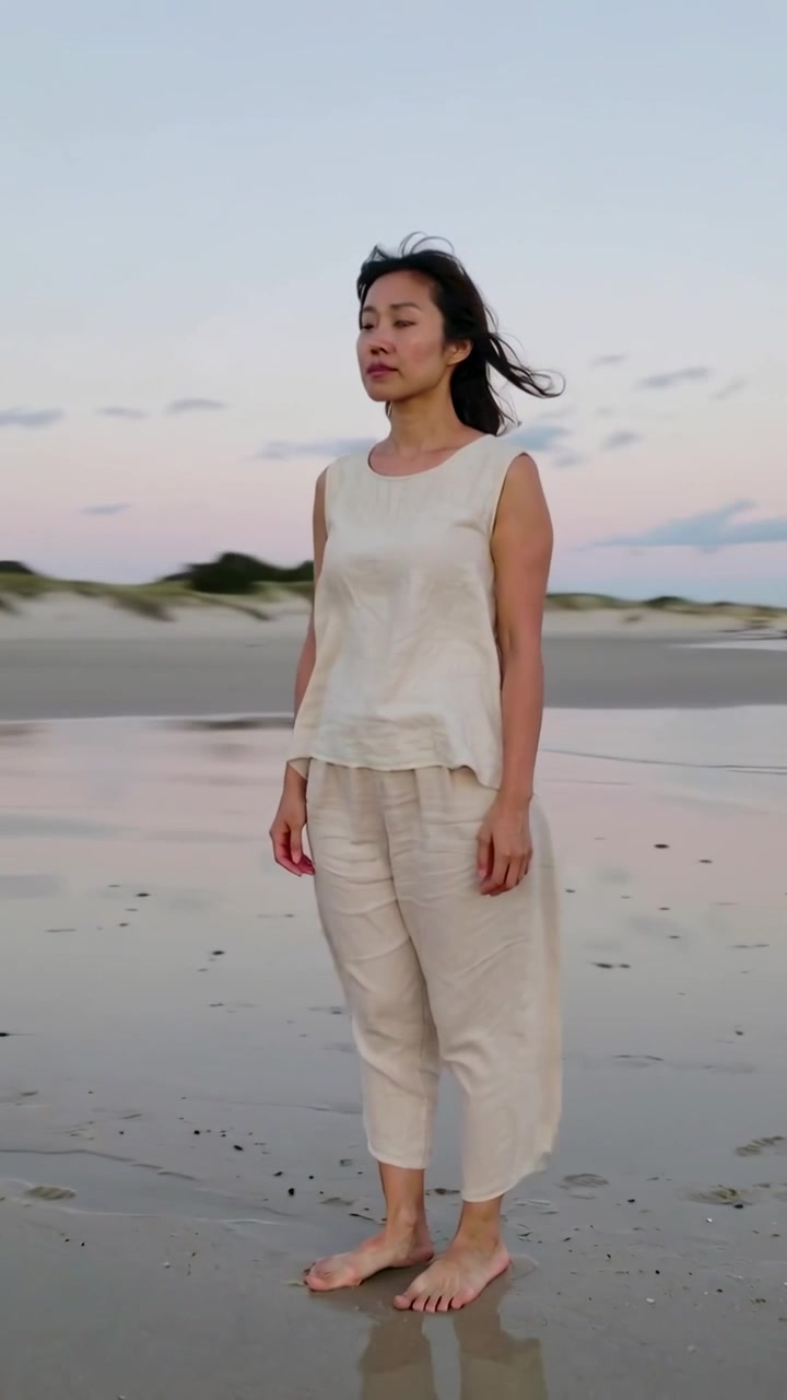 Video verticale: Donna che cammina a piedi nudi su una spiaggia al tramonto, la luce la fa fermare di fronte al mare, chiudendo gli occhi