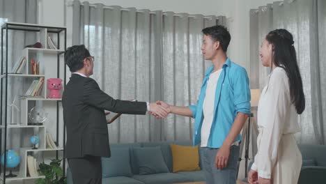 asian real estate agent shaking hands with a man who walks side by side a woman before talking about the house for sale