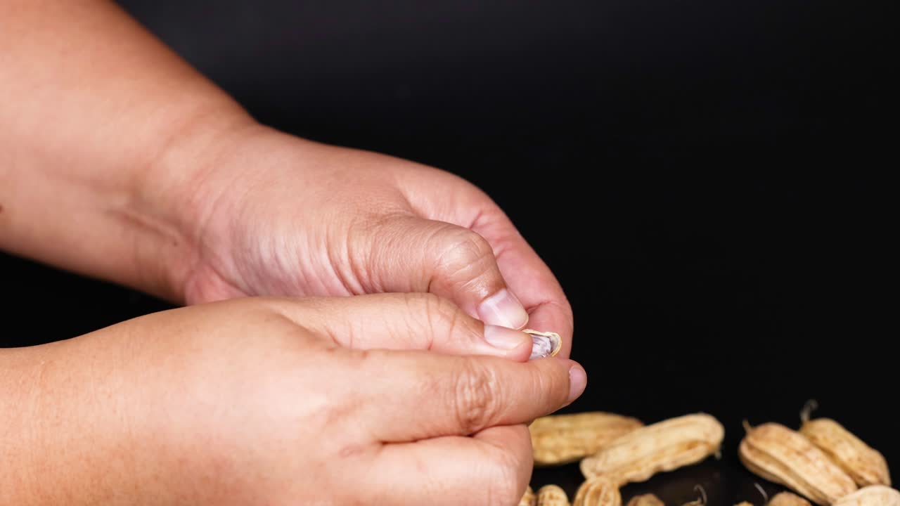 manos pelando cacahuetes en un fondo negro