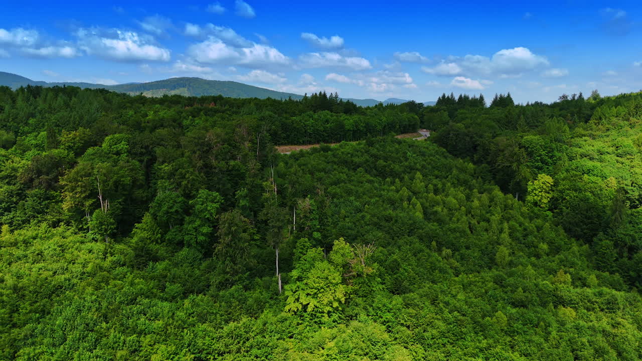 Lush green forests cover the vast mountainous area. Drone footage approaches the highway crossing the landscape