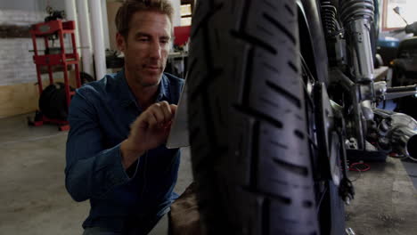 front view of caucasian male mechanic using digital tablet in motorbike repair garage 4k