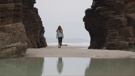 woman walking on a sandy beach between large rock formations