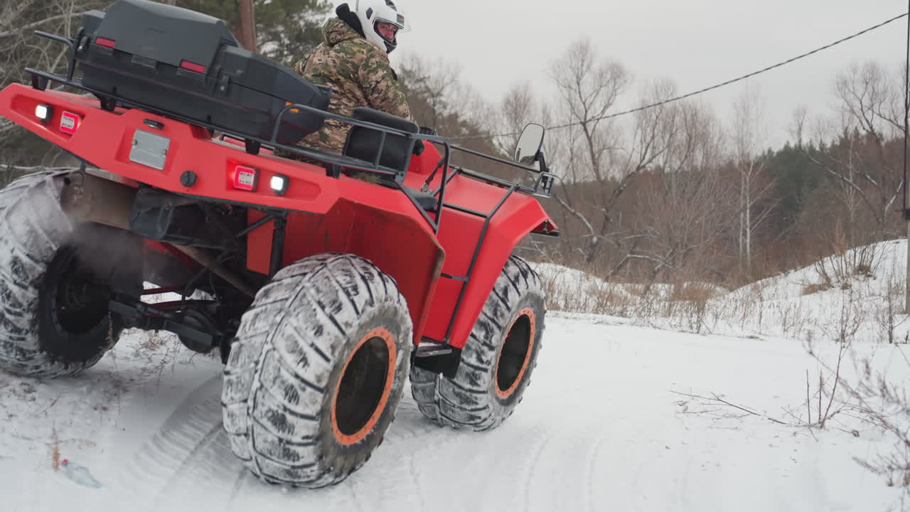 Rød ATV klatrer op ad stejl, sneklædt bakke, hjelmklædt rytter driver op ad bakken med forhjulene løftet og orangerandede dæk, der bider sig fast i det iskolde terræn, nærbillede af dækmønster og affjedring, aggressiv gasgivning og momentum.
