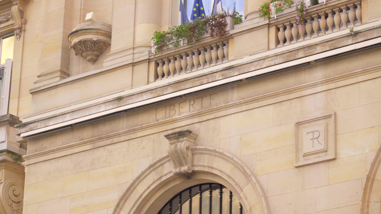 Uma imagem em close-up da palavra “Liberté” inscrita na fachada do Hôtel de Ville em Asnières-sur-Seine, exibindo a intrincada cantaria do século XIX sob a luz clara do dia.