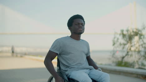 young black man riding in wheelchair along seashore