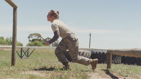 mujer soldado caucásica en forma va por encima y por debajo de los obstáculos en la carrera de obstáculos del ejército
