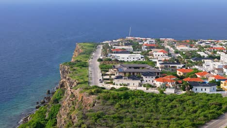 Vista-royal-homes-look-down-on-clear-blue-Caribbean-ocean-water,-catamaran-passing-by,-in-Curacao